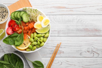 Delicious poke bowl with quail eggs, fish and edamame beans on white wooden table, flat lay. Space for text