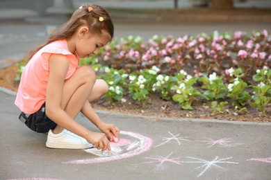 Photo of Little child drawing heart with chalk on asphalt