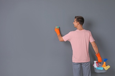 Man in gloves cleaning grey wall with sponge