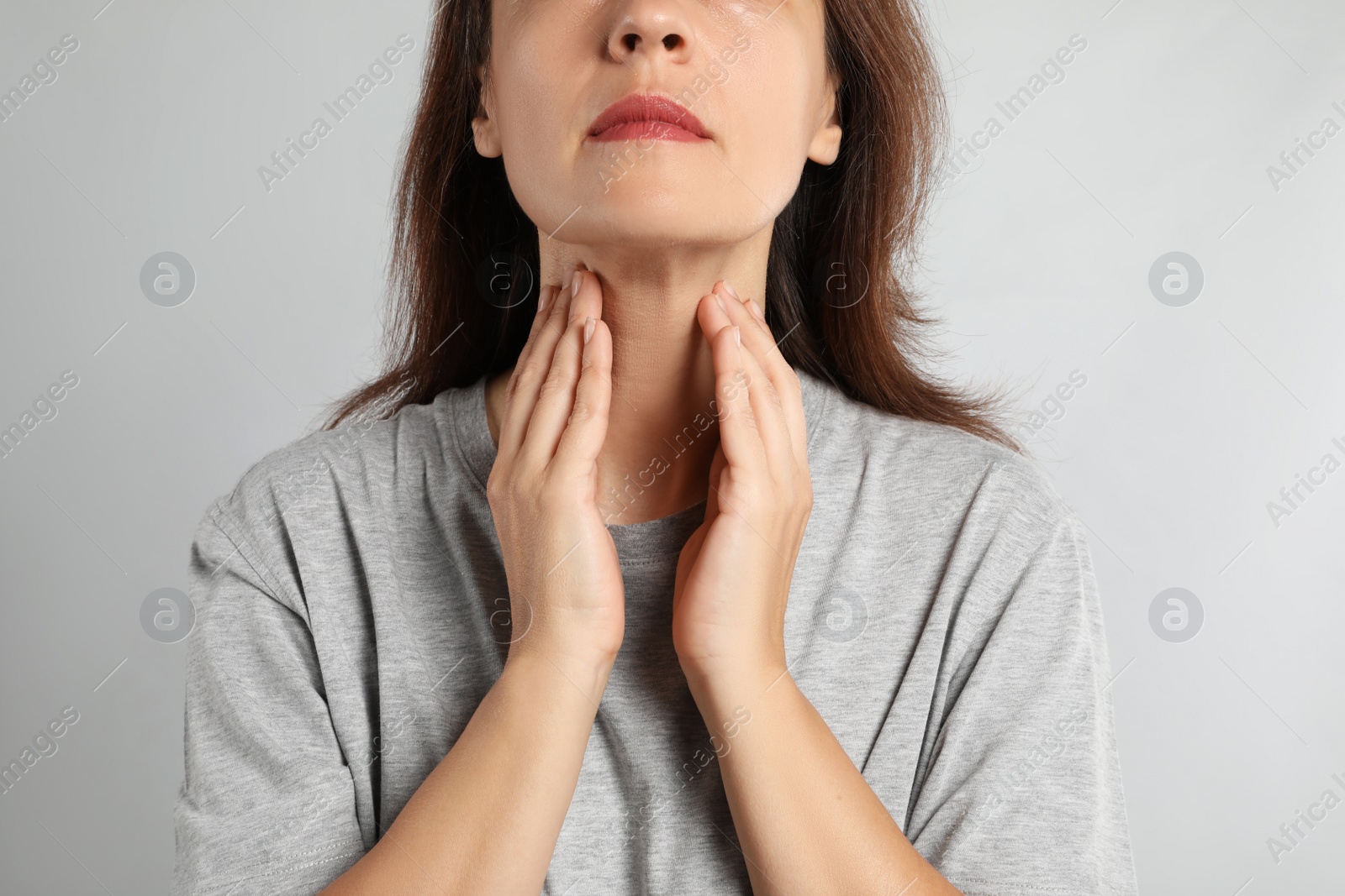 Photo of Mature woman doing thyroid self examination on light background, closeup