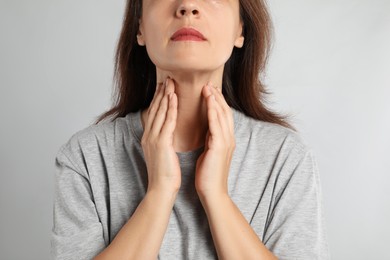 Mature woman doing thyroid self examination on light background, closeup