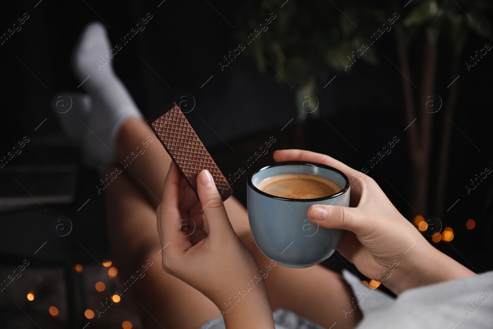 Photo of Woman with wafer and coffee on dark background, closeup. Early breakfast