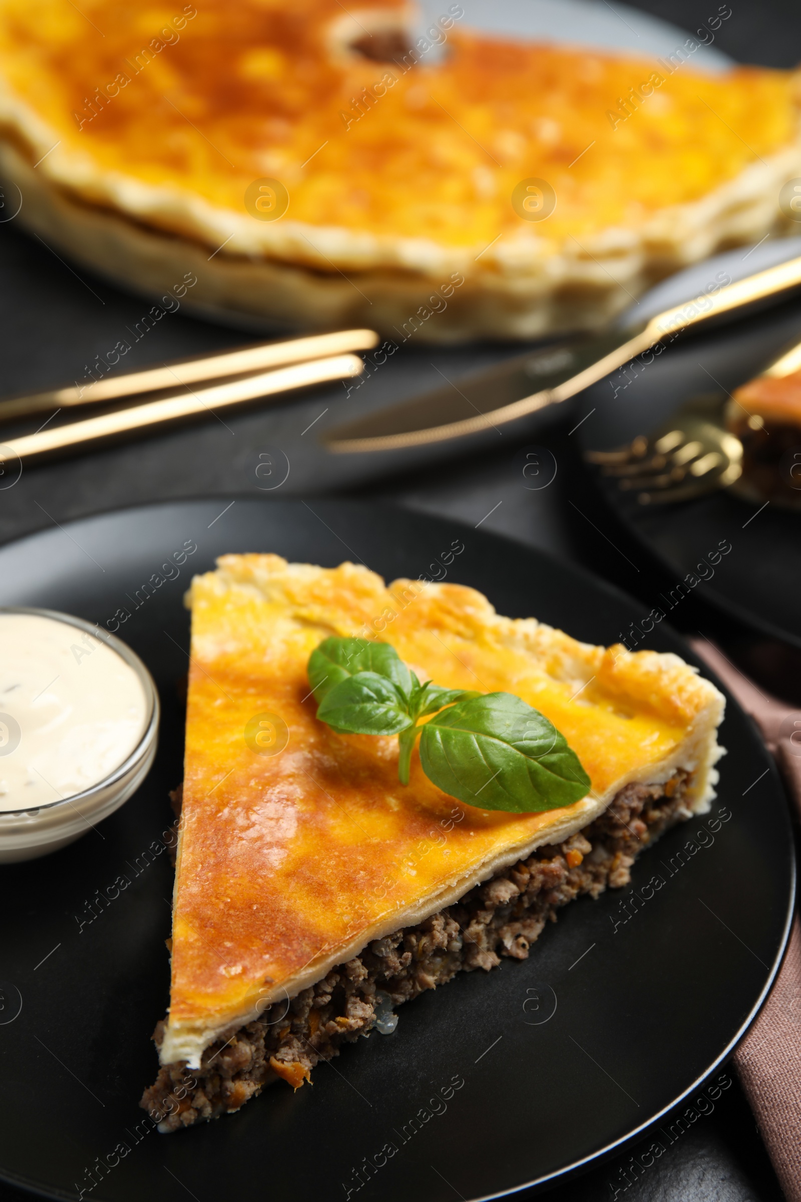 Photo of Piece of delicious pie with minced meat, basil and sauce served on table, closeup