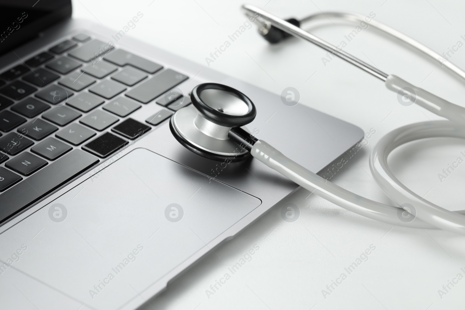 Photo of Modern laptop and stethoscope on white table, closeup