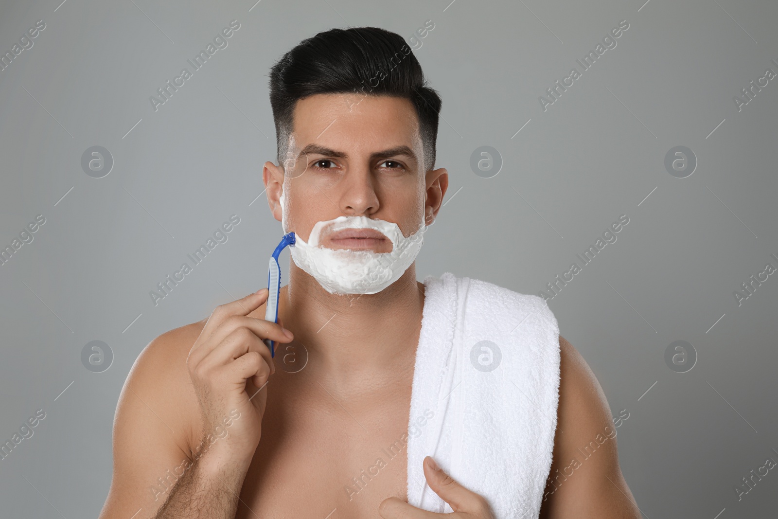 Photo of Handsome man shaving with razor on grey background