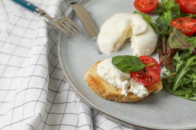 Photo of Delicious burrata cheese with tomatoes, arugula and toast served on checkered tablecloth, closeup