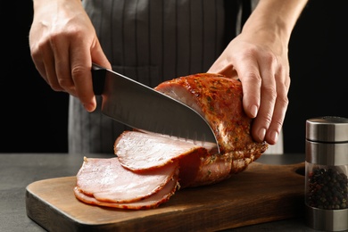 Woman cutting ham on wooden board at table, closeup