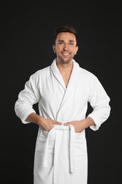 Happy young man in bathrobe on black background