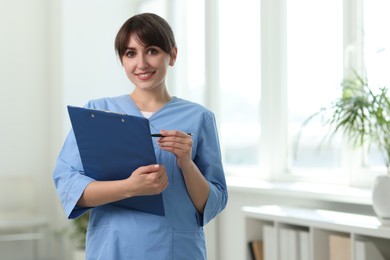 Portrait of smiling medical assistant with clipboard and pen in hospital. Space for text
