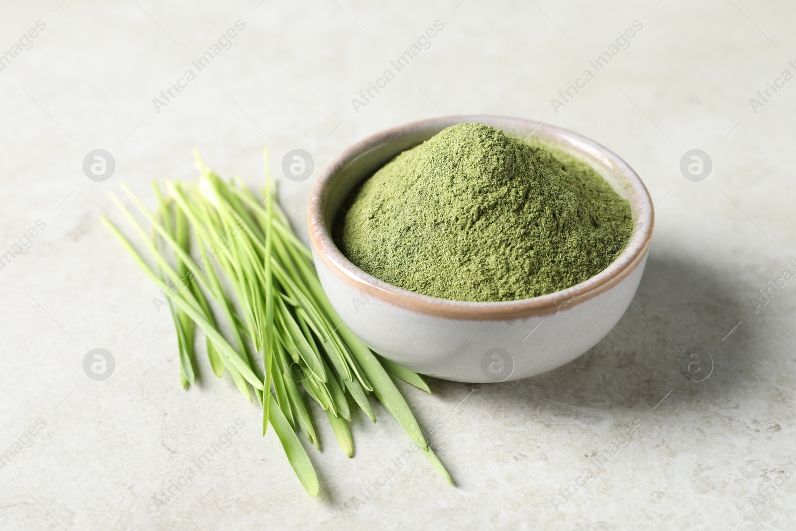 Photo of Wheat grass powder in bowl and fresh sprouts on light table