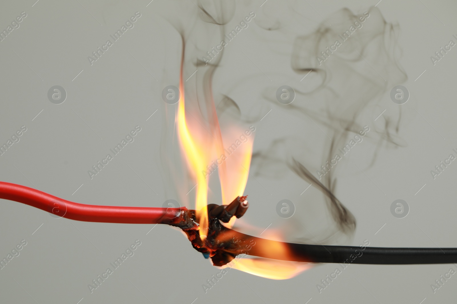 Photo of Inflamed red wire on grey background, closeup. Electrical short circuit