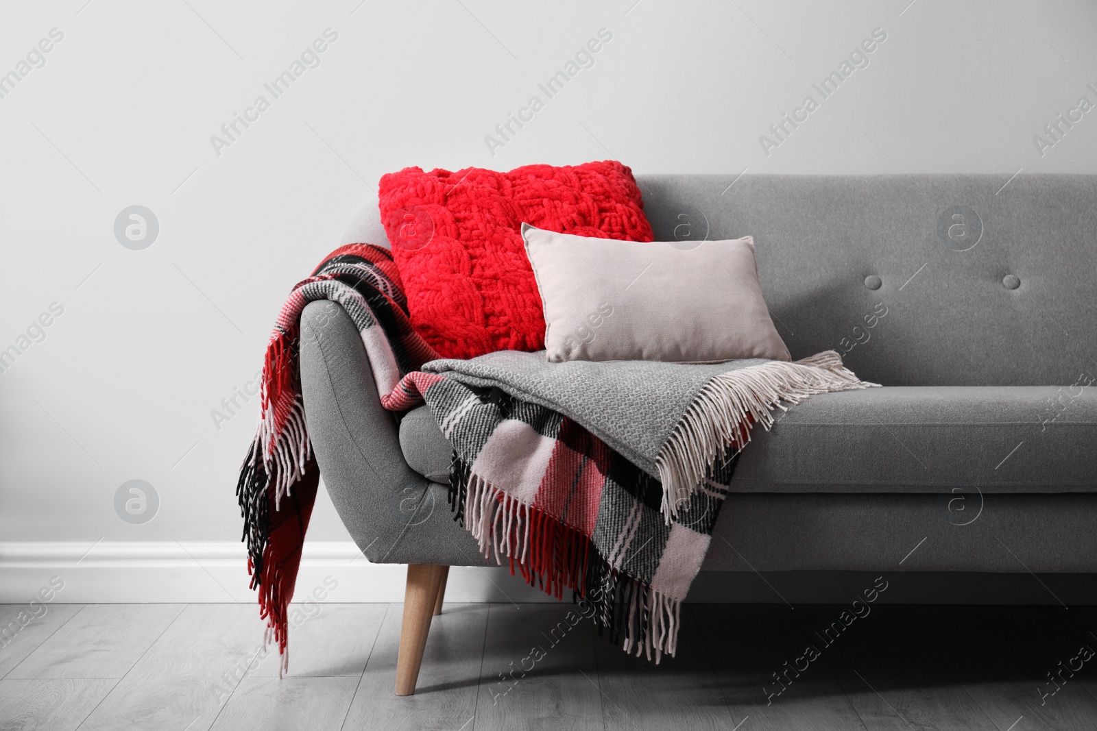 Photo of Sofa with soft pillows and warm plaids near light wall indoors