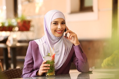 Photo of Muslim woman talking on phone in outdoor cafe