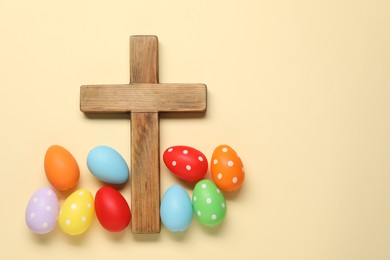 Wooden cross and painted Easter eggs on beige background, flat lay. Space for text