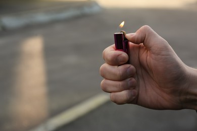 Photo of Man holding lighter with burning flame outdoors, closeup. Space for text