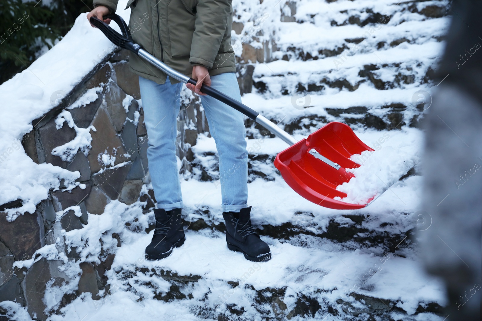 Photo of Man cleaning stairs from snow with shovel outdoors on winter day, closeup