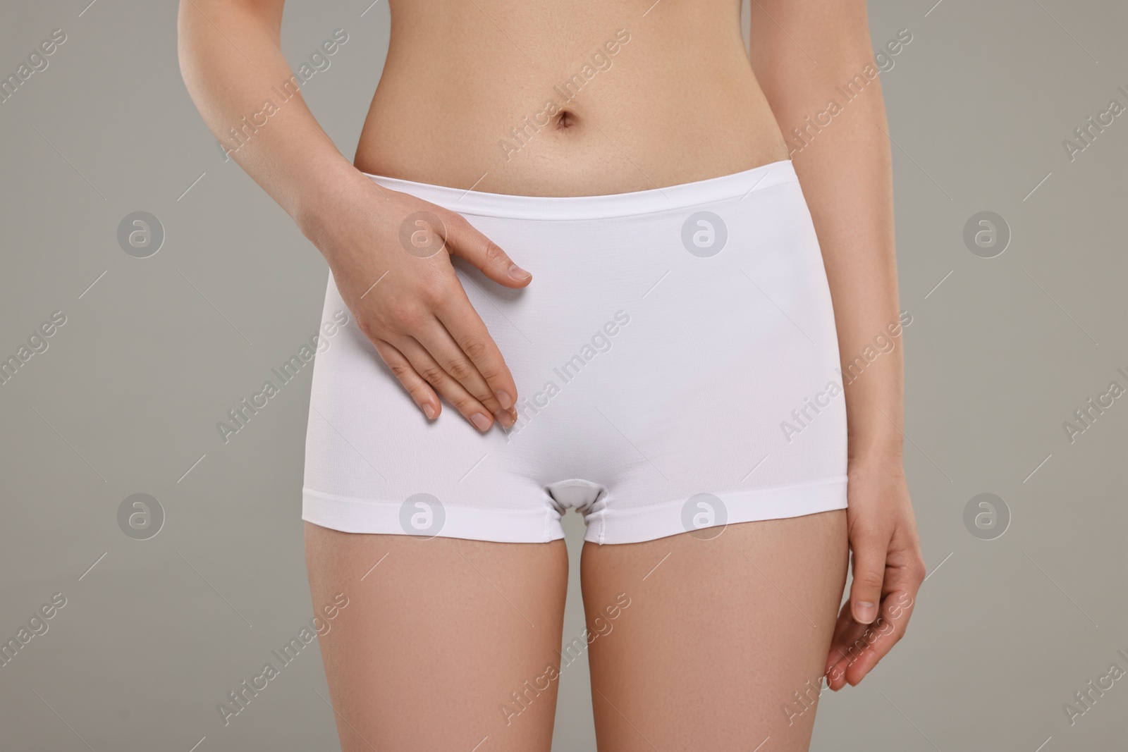 Photo of Woman holding hand near panties on grey background, closeup. Women's health