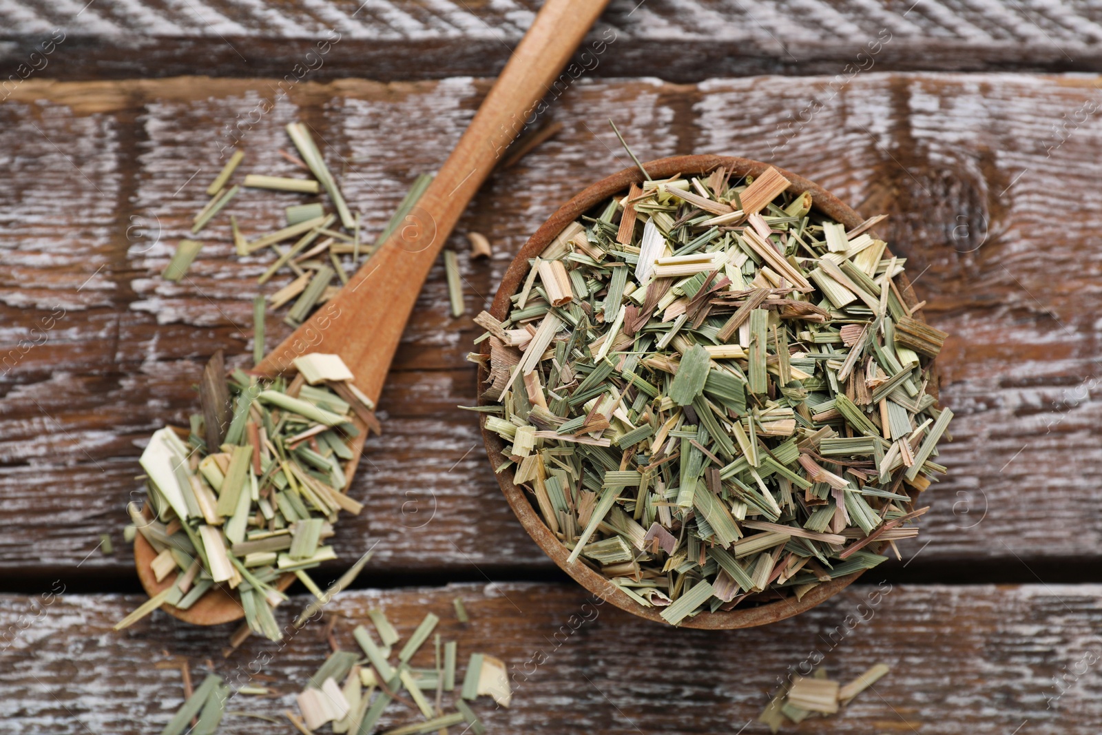 Photo of Bowl and spoon of aromatic dried lemongrass on wooden table, flat lay