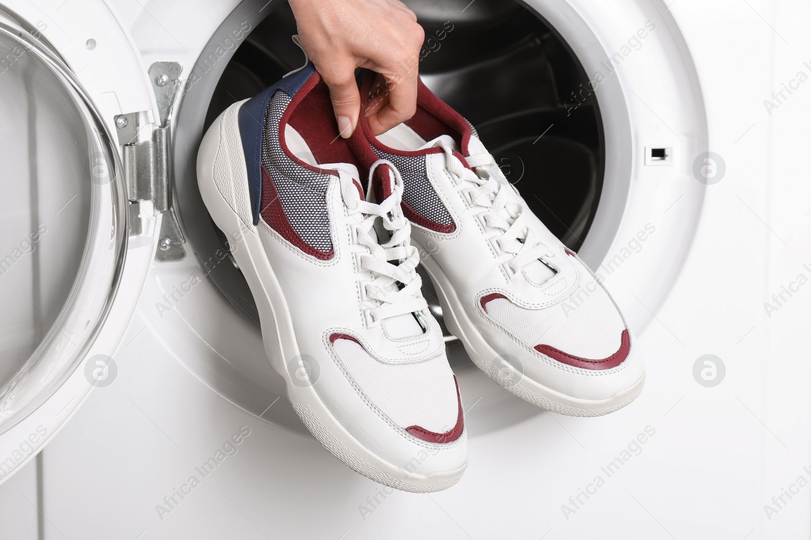 Photo of Woman putting pair of sport shoes into washing machine, closeup