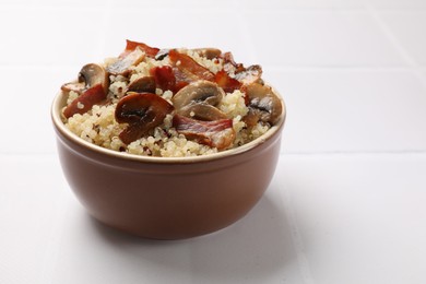 Tasty quinoa porridge with fried bacon and mushrooms in bowl on white table. Space for text