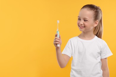 Photo of Happy girl holding electric toothbrush on yellow background. Space for text