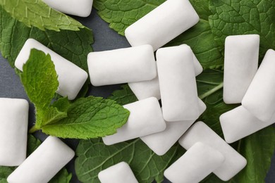 Photo of Tasty white chewing gums and mint leaves on grey background, flat lay
