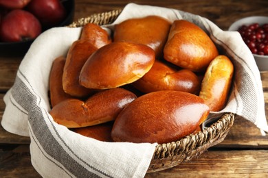 Delicious baked pirozhki in wicker basket on wooden table