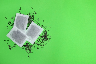 Photo of Tea bags with scattered dry leaves on color background, top view. Space for text