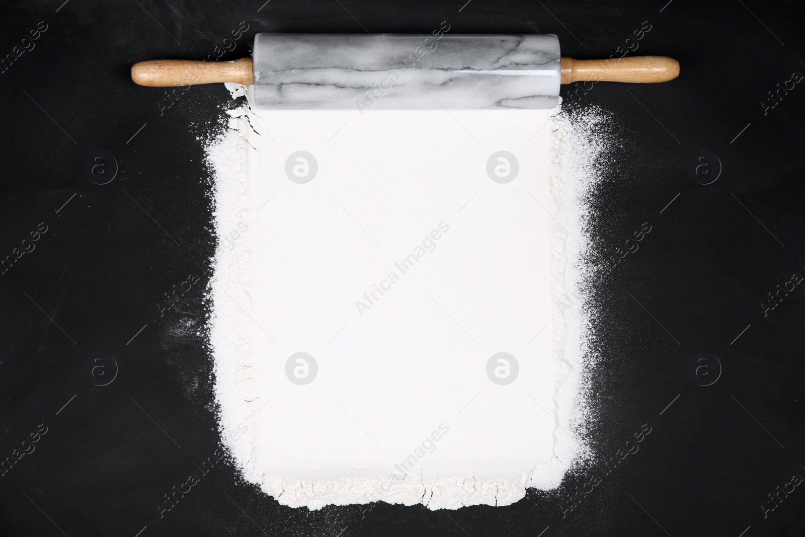 Photo of Flour and rolling pin on black table, flat lay