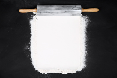 Photo of Flour and rolling pin on black table, flat lay