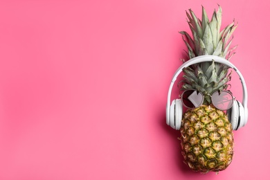 Photo of Top view of pineapple with headphones and sunglasses on pink background, space for text. Creative concept