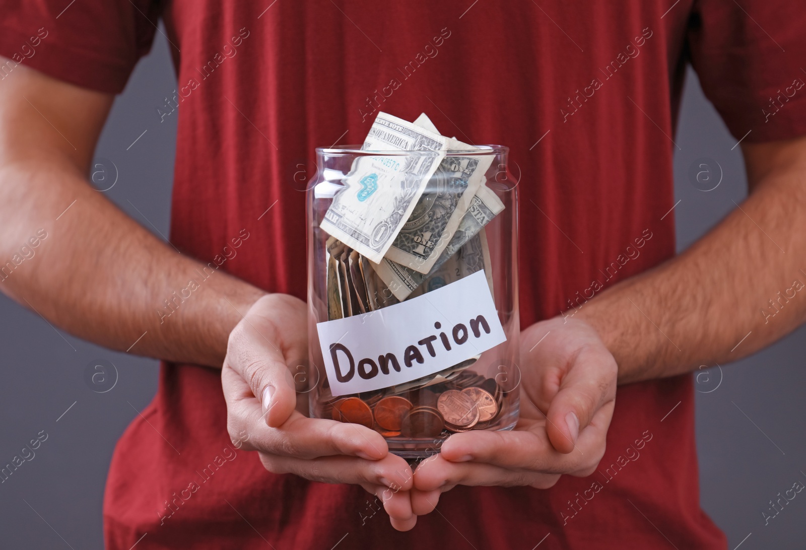 Photo of Man holding jar with money and label DONATION on grey background, closeup