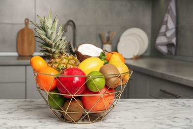 Metal basket with different ripe fruits on white marble table in kitchen. Space for text