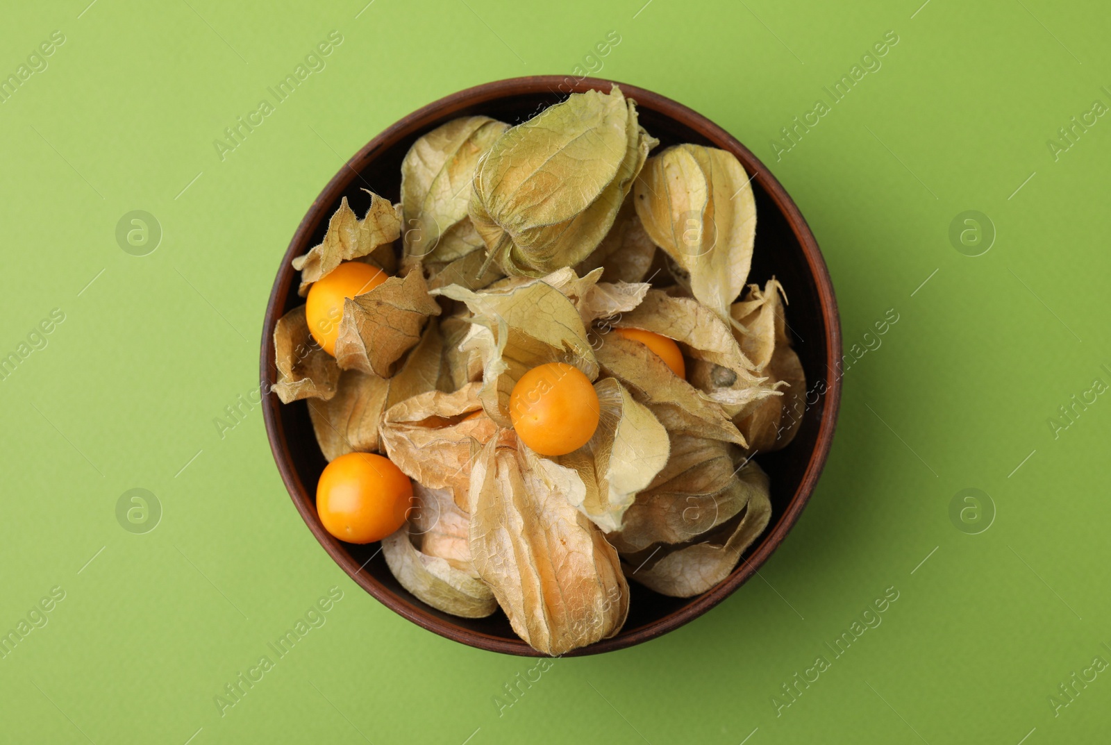 Photo of Ripe physalis fruits with calyxes in bowl on green background, top view