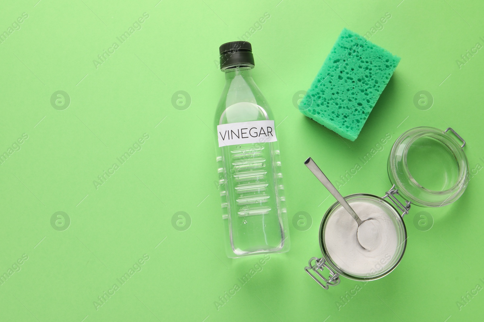 Photo of Eco friendly natural cleaners. Vinegar in bottle, sponge and jar of soda on green background, flat lay. Space for text