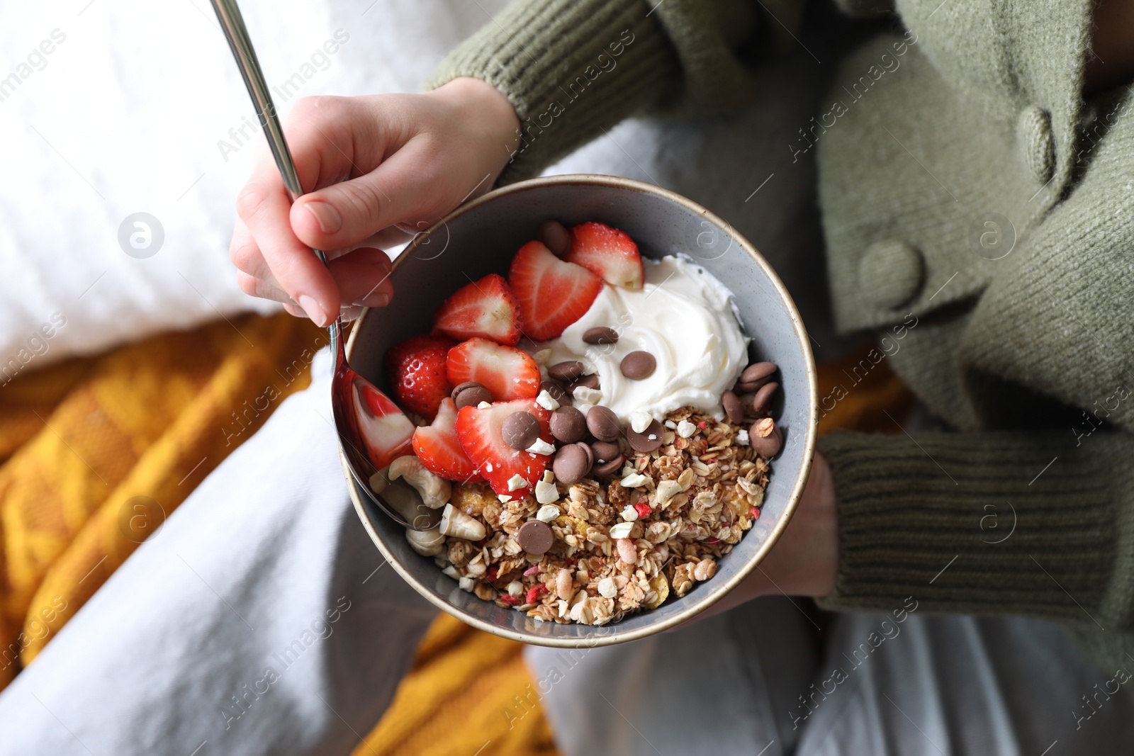 Photo of Woman eating tasty granola with chocolate chips, strawberries and yogurt indoors, top view