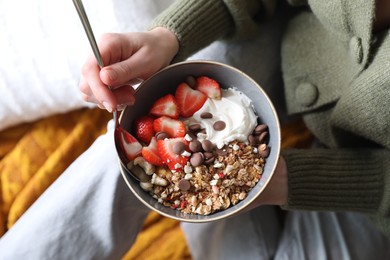 Woman eating tasty granola with chocolate chips, strawberries and yogurt indoors, top view