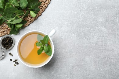 Cup of aromatic green tea with mint and dry leaves on grey table, flat lay. Space for text