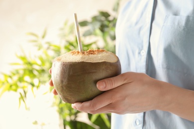 Young woman with fresh coconut cocktail on blurred background, closeup