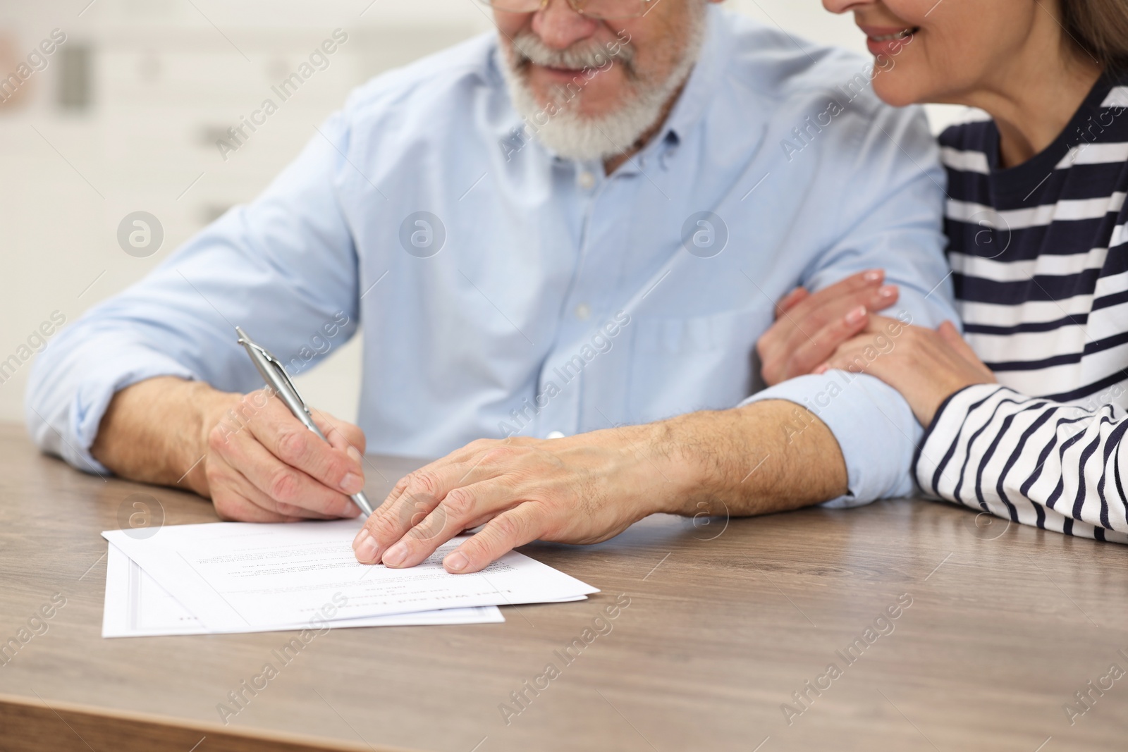 Photo of Happy senior couple signing Last Will and Testament at wooden table, closeup