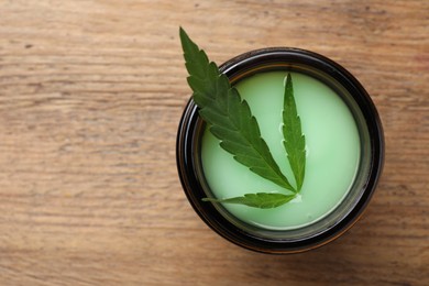 Jar of hemp cosmetics with green leaf on wooden table, top view. Space for text