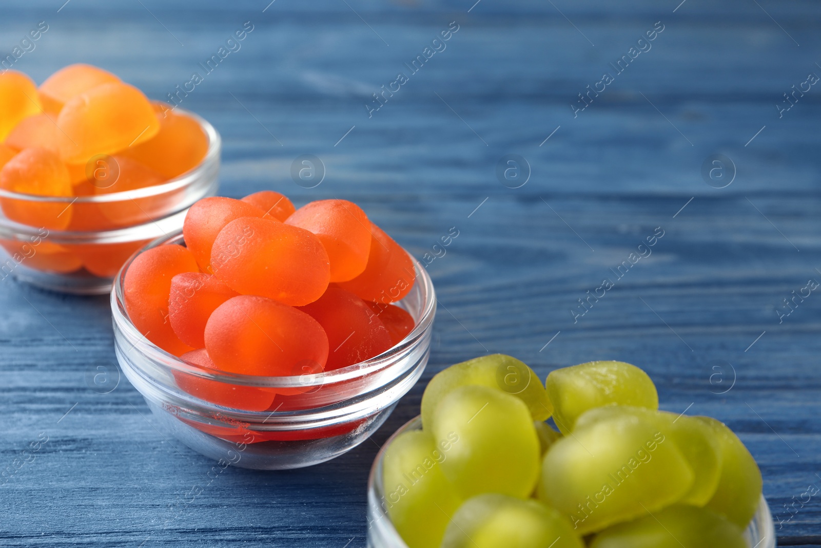 Photo of Glass bowls with tasty jelly candies on blue wooden table, space for text