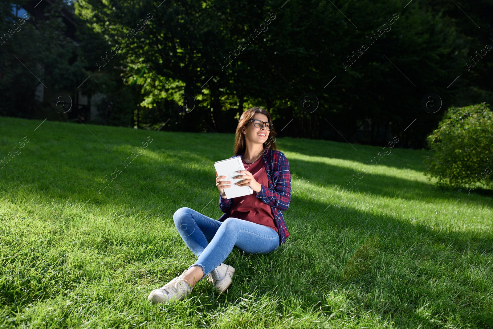 Photo of Young woman with book in park on sunny day
