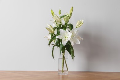 Photo of Beautiful bouquet of lily flowers in glass vase on floor near white wall
