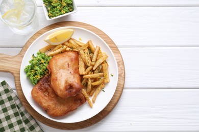 Photo of Tasty fish, chips, sauce, peas and lemon on white wooden table, top view. Space for text