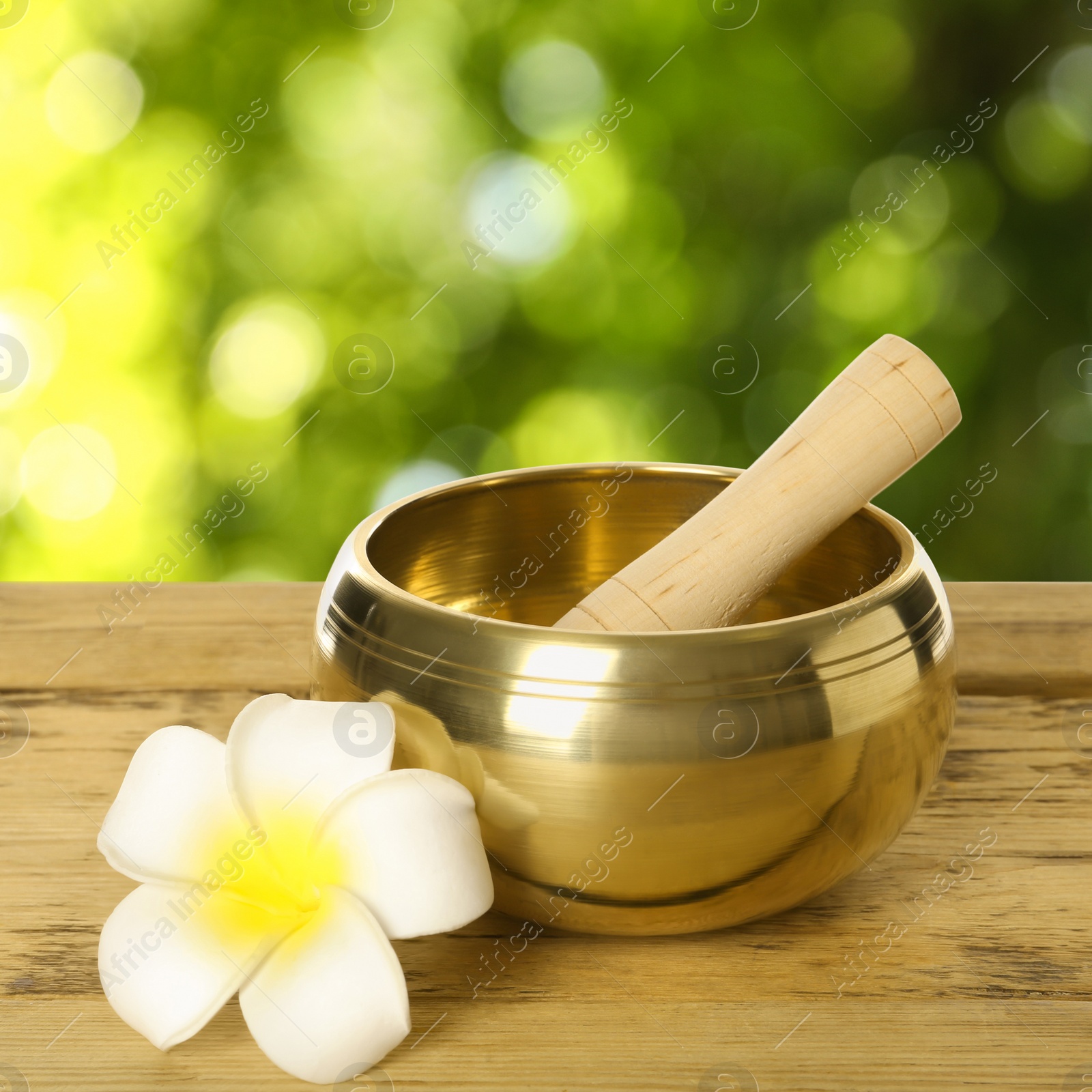 Image of Golden singing bowl, mallet and flower on wooden table outdoors. Bokeh effect 