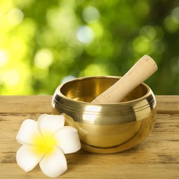 Image of Golden singing bowl, mallet and flower on wooden table outdoors. Bokeh effect 