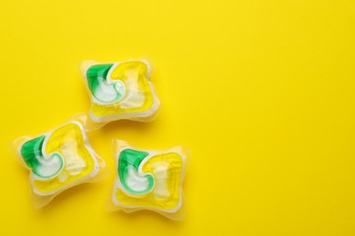 Photo of Dishwasher detergent pods on yellow background, flat lay. Space for text