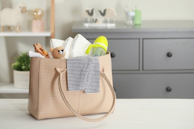 Photo of Mother's bag with baby's stuff on white wooden table indoors. Space for text