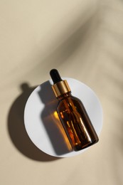 Bottle of cosmetic oil on beige background, top view